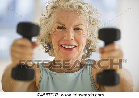 Stock Image - USA, New Jersey, Jersey City, Portrait of senior woman using hand weights at gym. Fotosearch