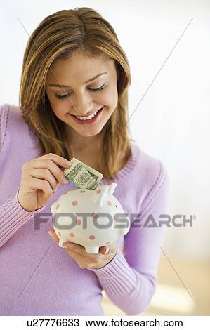 USA, New Jersey, Jersey City, Portrait of young woman putting banknote to piggybank View Large Photo Image Stock Image - USA, New Jersey, Jersey City, Portrait of young woman putting banknote to piggybank. Fotosearch