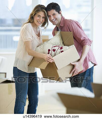 Stock Photo - USA, New Jersey, Jersey City, Portrait of couple carrying box in new home. Fotosearch