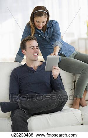Stock Photo - USA, New Jersey, Jersey City, Portrait of young couple sitting on sofa with digital tablet. Fotosearch