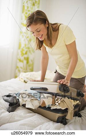 Stock Photo - USA, New Jersey, Jersey City, Portrait of young woman packing clothes. Fotosearch