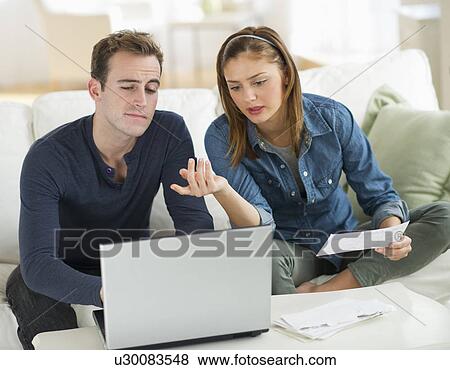 Stock Photo - USA, New Jersey, Jersey City, Portrait of young couple doing paperwork at home. Fotosearch