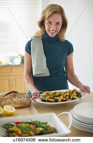 Stock Photograph - USA, New Jersey, Jersey City, Portrait of woman preparing food in kitchen. Fotosearch