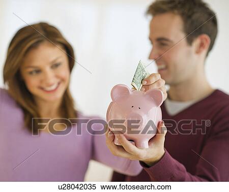 USA, New Jersey, Jersey City, Portrait of young couple putting banknote to piggybank View Large Photo Image Stock Photography - USA, New Jersey, Jersey City, Portrait of young couple putting banknote to piggybank. Fotosearch