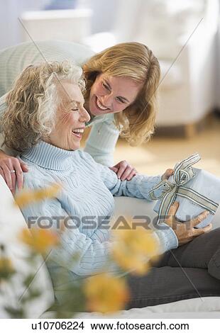 Picture - USA, New Jersey, Jersey City, Senior woman receiving present from daughter on sofa. Fotosearch