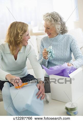 Stock Photograph - USA, New Jersey, Jersey City, Senior mother and daughter wrapping gifts in living room. Fotosearch