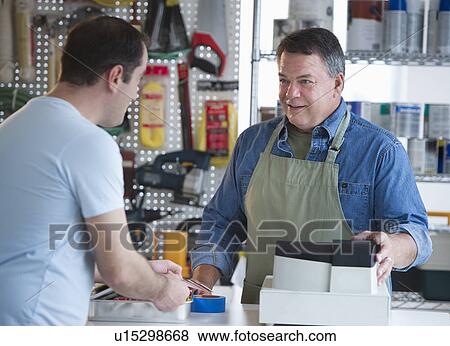 Stock Photo - USA, New Jersey, Jersey City, Shop owner serving customer in hardware shop. Fotosearch