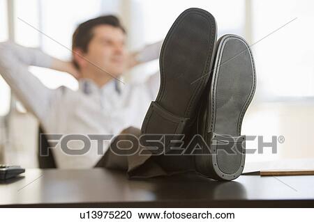 Stock Image - USA, New Jersey, Jersey City, Businessman with feet up on desk. Fotosearch