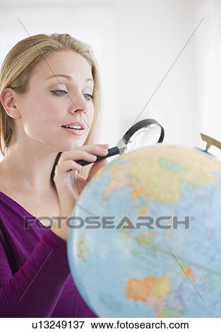 Stock Photo - USA, New Jersey, Jersey City, Attractive young woman examining globe with magnifying glass. Fotosearch
