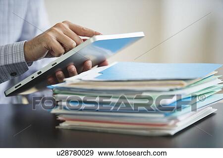 Stock Photo - USA, New Jersey, Jersey City, Businessman using digital tablet by paperwork. Fotosearch