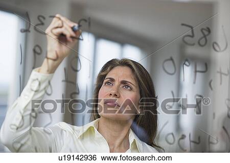 Stock Photograph - USA, New Jersey, Jersey City, Businesswoman writing calculations on glass. Fotosearch
