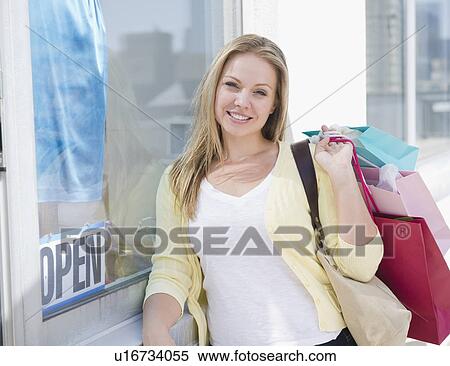 Stock Photography - USA, New Jersey, Jersey City, Attractive young woman emerging from shop with shopping bags. Fotosearch
