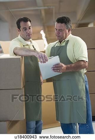 Stock Image - USA, New Jersey, Jersey City, Two male warehouse workers by stacked boxes. Fotosearch