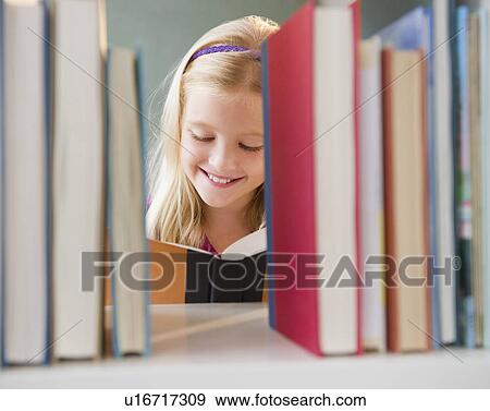 Stock Photo - USA, New Jersey, Jersey City, View across the shelf showing girl (8-9) reading book. Fotosearch
