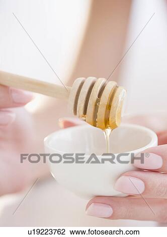 Stock Image - USA, New Jersey, Jersey City, Woman hand holding honey spoon. Fotosearch