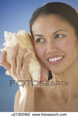 Stock Image - USA, New Jersey, Jersey City, Woman listening to conch shell. Fotosearch