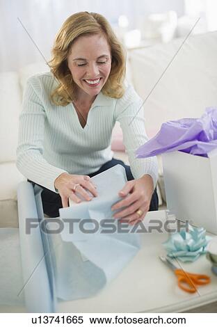 Stock Photography - USA, New Jersey, Jersey City, Woman wrapping gifts in living room. Fotosearch