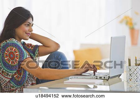 Stock Image - USA, New Jersey, Jersey City, Young Indian woman using laptop. Fotosearch