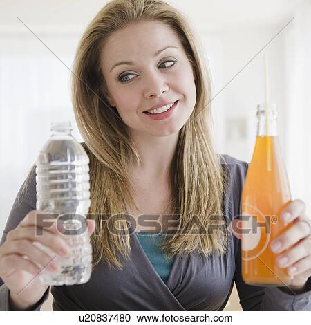 USA, New Jersey, Jersey City, Young woman trying to choose between organic juice and mineral water View Large Photo Image Stock Image - USA, New Jersey, Jersey City, Young woman trying to choose between organic juice and mineral water. Fotosearch