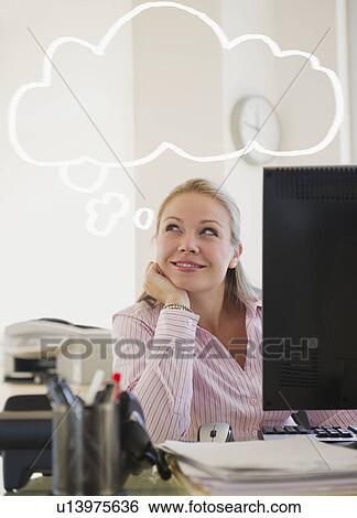 Stock Photograph - USA, New Jersey, Jersey City, Young attractive businesswoman daydreaming in office. Fotosearch