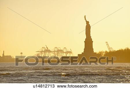 Stock Image - USA, New York City, Staten Island, Harbor and silhouette of Statue of Liberty in background. Fotosearch