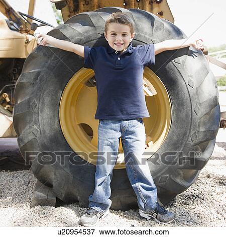 Stock Photo - USA, New York, Flanders, Boy (4-5) standing in front of tractor wheel. Fotosearch