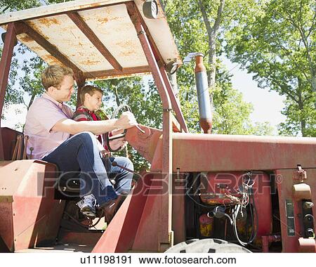 Stock Image - USA, New York, Flanders, Boy (8-9) with father sitting on tractor. Fotosearch