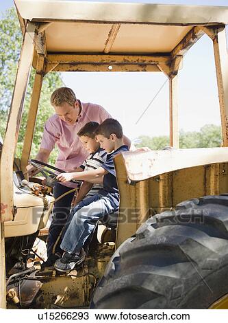 Stock Image - USA, New York, Flanders, Two boys (4-5, 8-9) with father sitting on tractor. Fotosearch