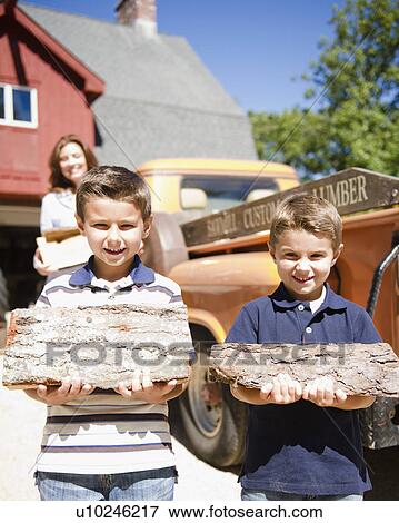 Stock Photo - USA, New York, Flanders, Two boys (4-5, 8-9) holding firewood. Fotosearch