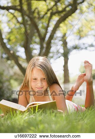 Stock Image - USA, New York, Girl (10-11) reading book in park. Fotosearch