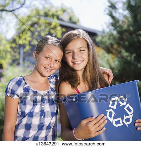 Stock Image - USA, New York, Two girls (10-11, 10-11) holding recycling bin. Fotosearch