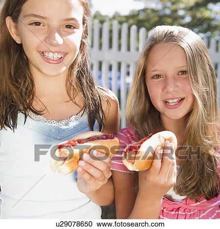 Stock Image - USA, New York, Two girls (10-11, 10-11) eating hot-dogs. Fotosearch