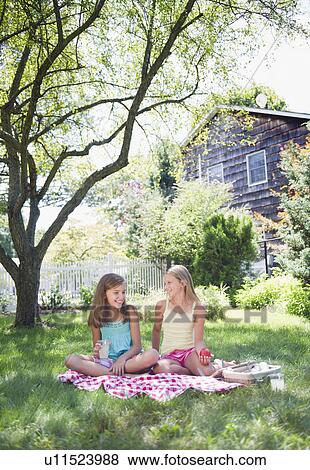 Stock Photo - USA, New York, Two girls (10-11, 10-11) sitting on blanket in backyard. Fotosearch