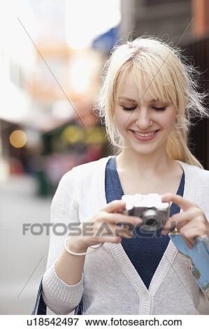 Stock Photo - USA, Seattle, Smiling young woman holding digital camera. Fotosearch