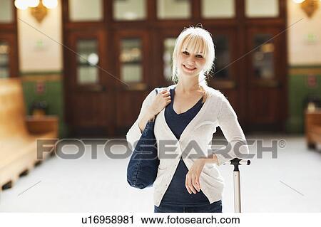 Stock Image - USA, Seattle, Young woman at train station standing with luggage and looking at camera. Fotosearch