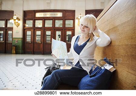 Stock Image - USA, Seattle, Young woman sitting at train station and reading map. Fotosearch