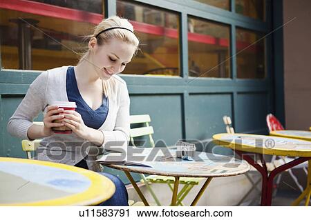 Stock Image - USA, Seattle, Young woman sitting with coffee and reading map. Fotosearch