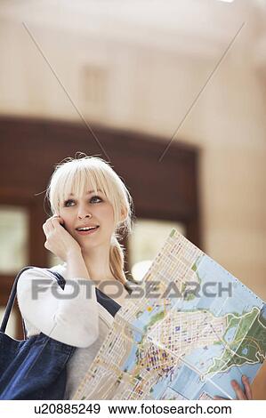 Stock Photo - USA, Seattle, Young woman talking via phone and holding map. Fotosearch