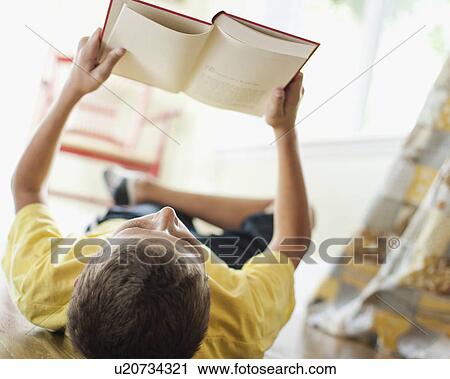 Stock Image - USA, Utah, Boy (10-11) reading book on floor. Fotosearch