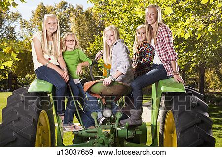 Stock Photo - USA, Utah, family portrait of sisters (6-7, 8-9, 12-13, 14-15, 16-17) sitting on tractor. Fotosearch