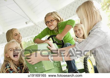 Stock Photography - USA, Utah, family portrait of sisters (6-7, 8-9, 12-13, 14-15, 16-17) at table playing with tractor toy. Fotosearch