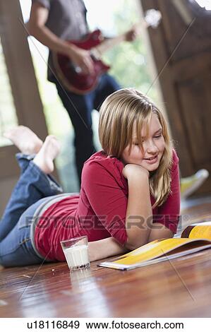 Stock Photo - USA, Utah, Girl (10-11) reading magazine while man in the background playing guitar. Fotosearch