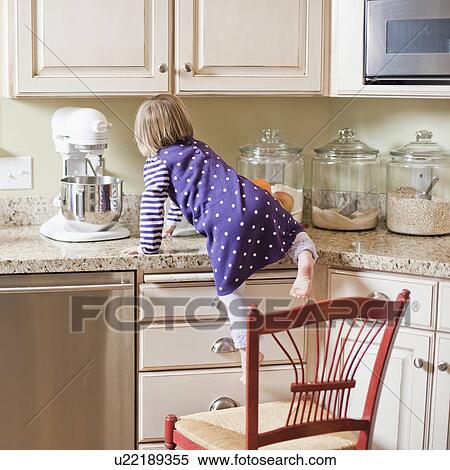 Stock Photography - USA, Utah, Girl (2-3) climbing on cupboard in kitchen. Fotosearch