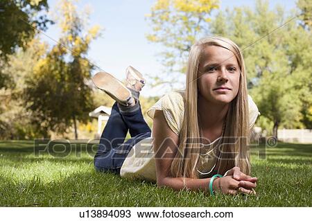 Stock Image - USA, Utah, outdoor of blonde girl (12-13) lying on grass. Fotosearch