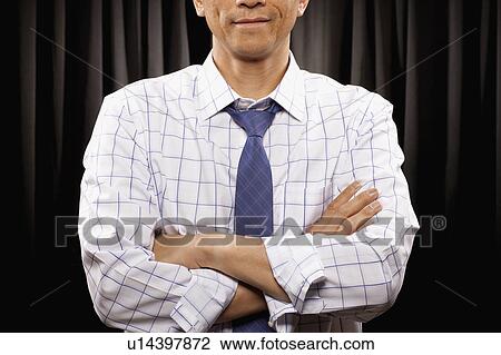 Stock Image - USA, Utah, Provo, Man with arms crossed standing in front of black curtain, mid section. Fotosearch