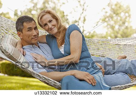 Stock Image - USA, Utah, Provo, Portrait of smiling mature couple relaxing in hammock in garden. Fotosearch