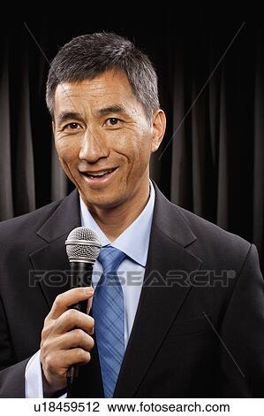 Stock Image - USA, Utah, Provo, Portrait of businessman with microphone standing in front of black curtain. Fotosearch