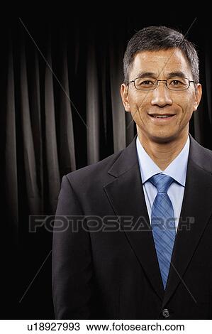 Stock Image - USA, Utah, Provo, Portrait of businessman standing in front of black curtain. Fotosearch