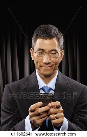 Stock Image - USA, Utah, Provo, Smiling businessman standing in front of black curtain and text messaging. Fotosearch