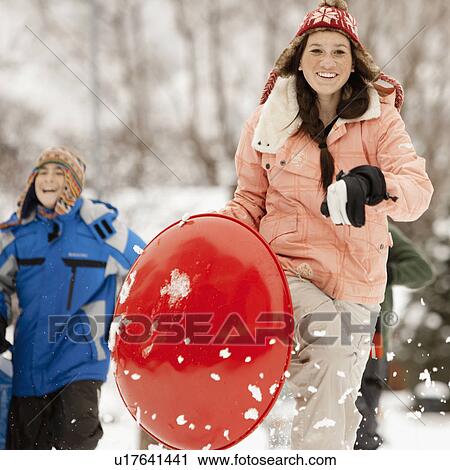 Stock Image - USA, Utah, Provo, Teenage (16-17) girl running with sledge, boys and girls (10-11, 12-13) in background. Fotosearch